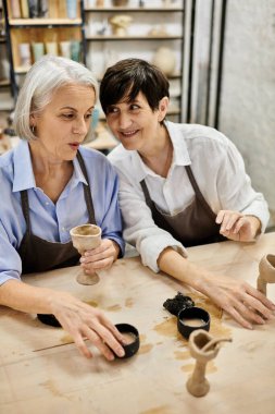 İki kadın, olgun bir lezbiyen çift, çömlekçilik kursunda, el işi yapıyor ve gülüyorlar..