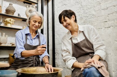 İki yetişkin kadın samimi bir stüdyoda çömlekçilik üzerinde birlikte çalışıyor..