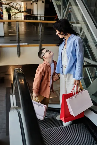 Down sendromlu bir anne ve oğlu alışveriş merkezinde alışveriş yapıyor, yürüyen merdivende birlikte yürüyorlar..