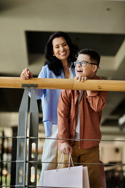A mother and her son with Down syndrome smile and laugh together while walking through a shopping mall.