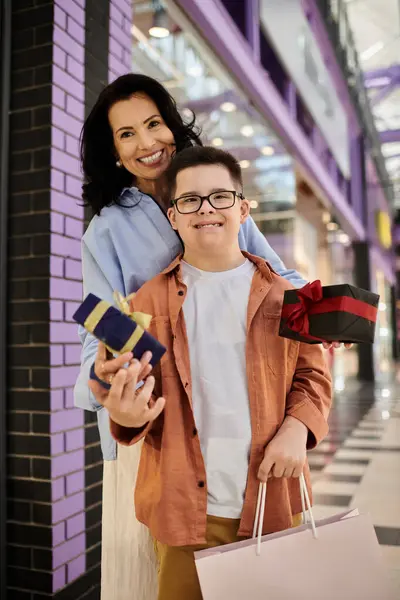 stock image A mother and her son with Down syndrome are walking through a shopping mall together, holding gifts.