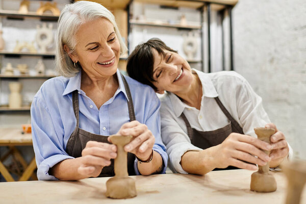Two mature women happily craft pottery together in a cozy art studio.