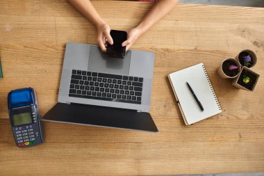 Önlüklü bir kadın, atölyesinde dizüstü bilgisayarıyla çalışıyor. Telefonunu kontrol ediyor..