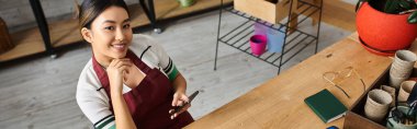 Asyalı bir kadın, küçük bir fabrika sahibi, işe ara verip, telefonuna dikkatlice bakıyor..