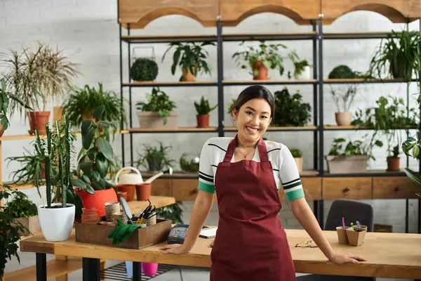 Genç Asyalı bir kadın, bir fabrika sahibi, dükkanında çalışırken sıcak bir şekilde gülümsüyor, çevresi canlı yeşilliklerle çevrili..