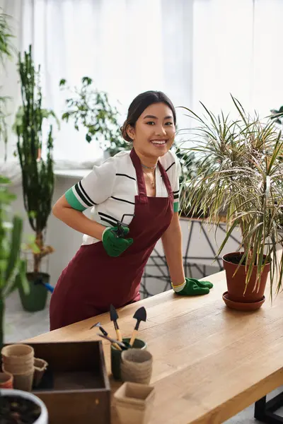 stock image A young Asian woman, wearing an apron, smiles while working in her plant store.