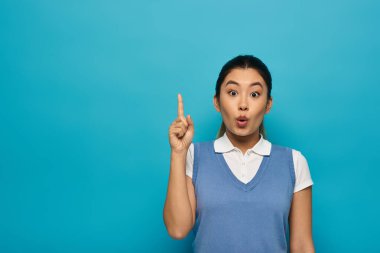 A young Asian woman in smart casual attire looks surprised with a raised finger, appearing to have just had a brilliant idea. clipart