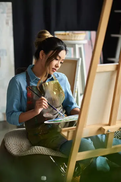 stock image A young Asian artist paints in her workshop, focused on creating a masterpiece.