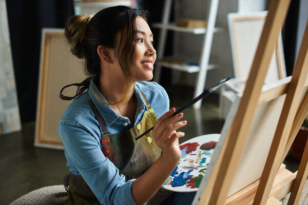 Молодая женщина в фартуке рисует кистью в руке в мастерской.
