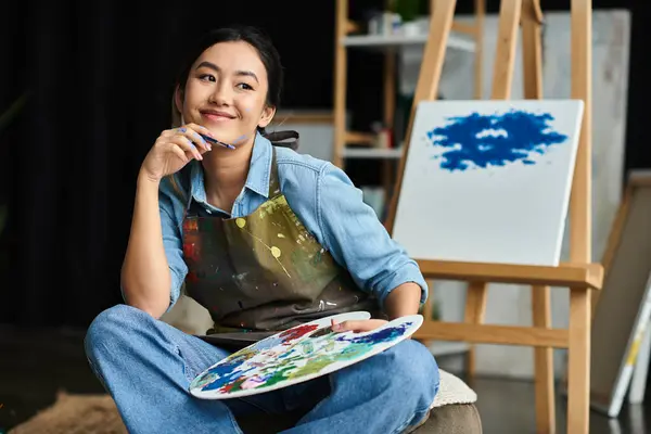 stock image A young woman, wearing an apron, contemplates her next brushstroke in her art studio.