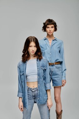 Kot giymiş iki genç kadın gri bir arkaplanda poz veriyor. Lezbiyen çift