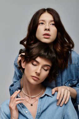 Kot gömlek giyen iki genç kadın, gri arka planda bir portre için poz veriyorlar..