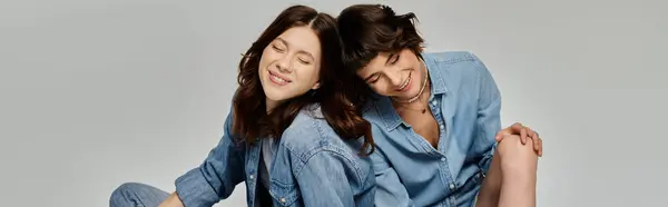 stock image A young lesbian couple, both wearing denim, poses for a photo shoot against a gray backdrop.