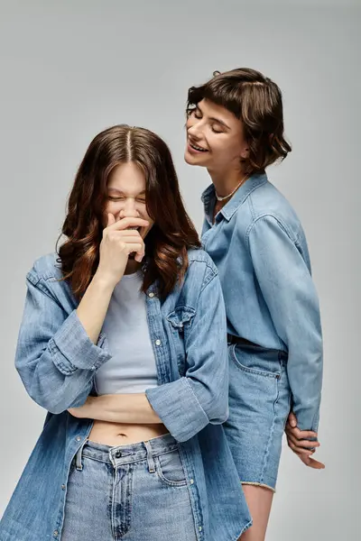 stock image Two young women dressed in denim stand and pose in a studio. They are laughing and smiling, showcasing their stylish fashion.