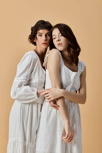 stock image Two young women in white summer dresses stand close together against a beige background. Lesbian couple