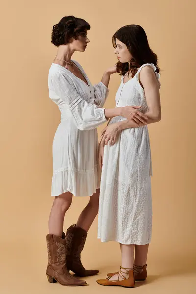 stock image Two women in white summer dresses pose against a beige background, showcasing a stylish and romantic lesbian couple.