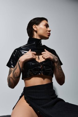 Siyah seksi elbiseli genç bir kadın beyaz bir duvara karşı poz veriyor..