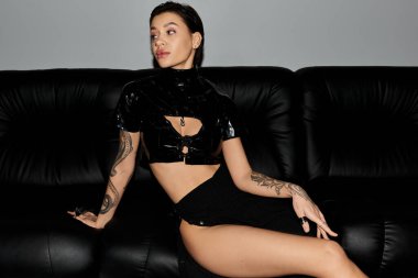 Siyah seksi giyinmiş genç bir kadın siyah deri bir koltukta baştan çıkarıcı pozlar veriyor..