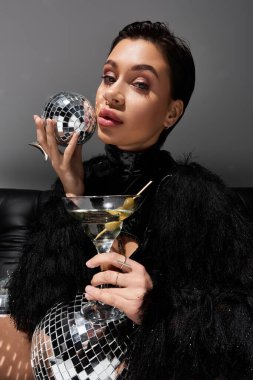 Seksi giyinmiş bir kadın elinde bir disko topu ve bir martini bardağıyla poz verir..