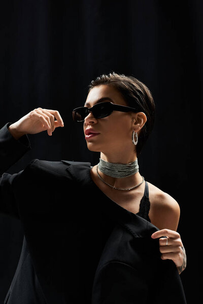 Женщина в солнечных очках и в блейзере позирует для фото.