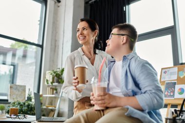 Bir anne, Down sendromu olan oğluna gülümserken modern ofis ortamında birlikte içki içmenin keyfini çıkarıyor..