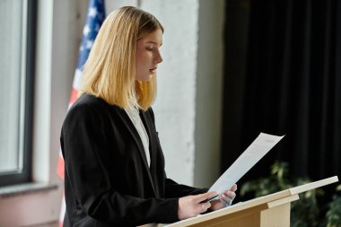 Teenage girl stands at a podium, delivering a speech at a Model United Nations conference. clipart