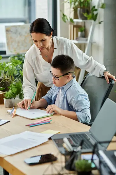 stock image A mother helps her son, who has Down syndrome, with an art project while working in her office.