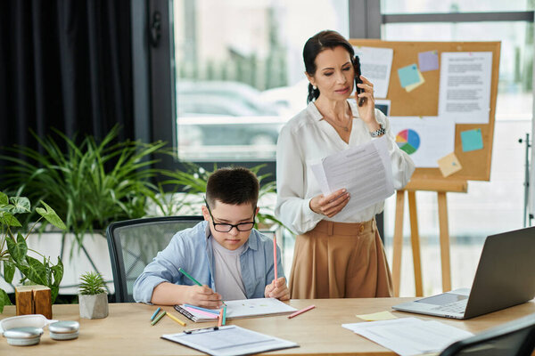 A mother works in her home office while her son with Down syndrome sits at the table, coloring.