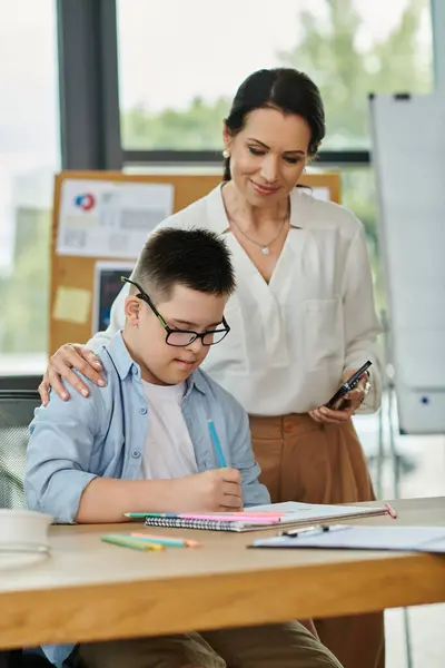 stock image A mother gently places her hand on her sons shoulder while he focuses on his work at a desk.