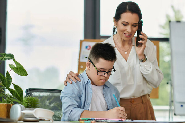 Мать работает в офисе, в то время как сын с синдромом Дауна учится поблизости, подчеркивая инклюзивность и поддержку на рабочем месте.