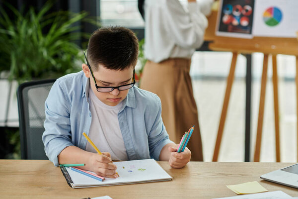 Мальчик с синдромом Дауна рисует за столом, пока его мать работает на заднем плане..