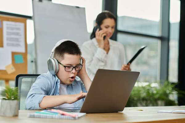 A boy with Down syndrome uses a laptop as his mother works nearby, showing inclusivity in a modern office.
