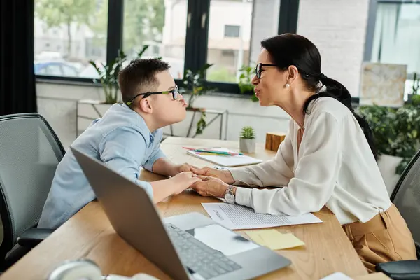 stock image A mother works in her home office next to her son with Down Syndrome, demonstrating diversity and inclusion.