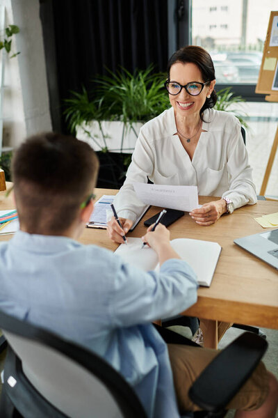A mother and her son with Down syndrome work together at a desk, showcasing inclusion and diversity in the workplace.