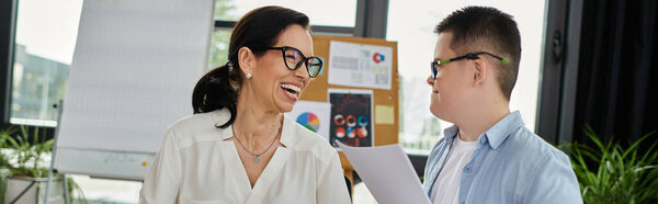 A mother smiles at her son, who has Down syndrome, while they work together in an office.