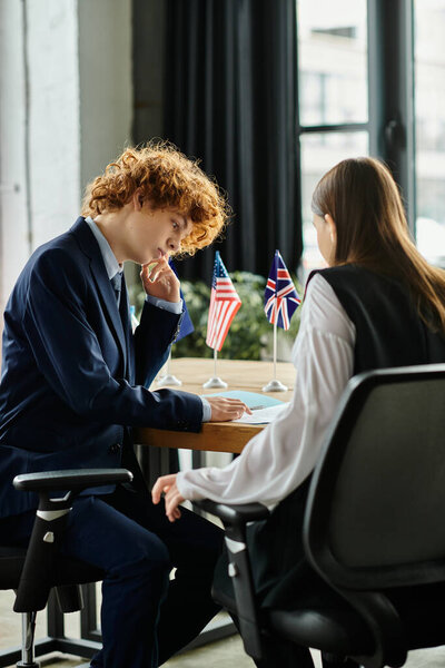 Два подростка погружаются в модель конференции ООН, изучая документ с флагами на заднем плане.