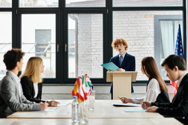 Подростки внимательно слушают на модельной конференции ООН, когда сверстник выступает с речью.