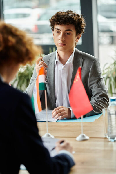 Подросток участвует в моделировании модели ООН, представляя страну с флагом на столе.
