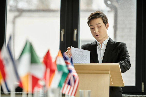 Teenage boy giving speech at Model UN, surrounded by flags.
