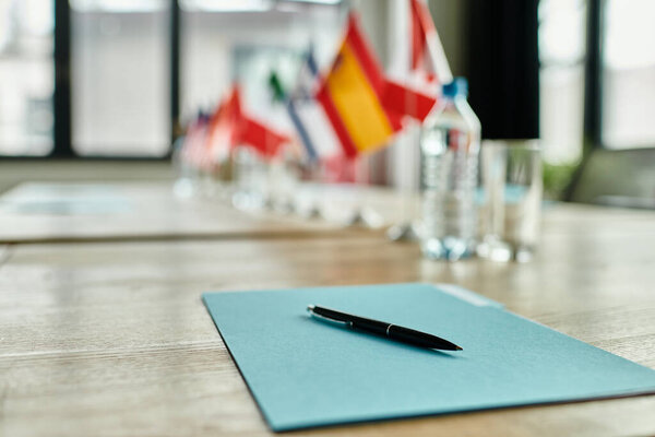 Ручка лежит на голубой папке, ожидая следующего раунда обсуждения на модельной конференции ООН.