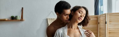 Genç bir Asyalı kadın ve Afrikalı bir Amerikalı erkek, yatak odası ortamında tutkulu bir kucaklaşmayı paylaşıyor..