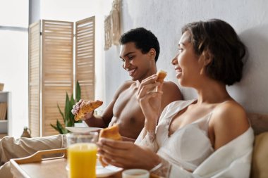 Genç, çok kültürlü bir çift yatak odalarında rahat ve samimi bir kahvaltı yapıyor..