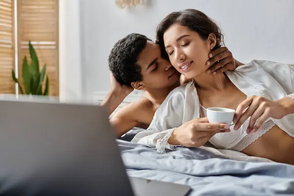 stock image A young couple enjoys a relaxing morning in bed, sharing a cup of coffee and a tender moment.