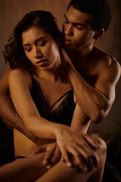 stock image Passionate couple embraces on a bed, displaying love and intimacy. Woman in black lingerie seduces partner with a sensual gaze.