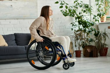 Tekerlekli sandalyedeki genç bir kadın evde oturup pencereden dışarı bakıyor..