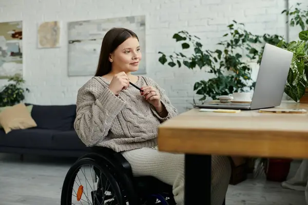 stock image A young woman in a wheelchair sits at a table in her home, pen in hand, reflecting on the day.