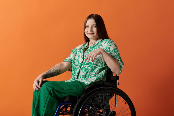 A young woman with long brown hair smiles confidently while sitting in a wheelchair against an orange background.
