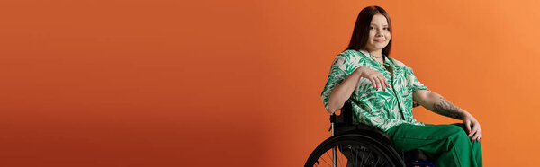 A young woman, dressed in a vibrant green shirt and pants, sits confidently in a wheelchair against an orange background.