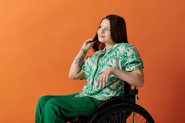 A young woman in a vibrant green and white shirt sits in a wheelchair against an orange background, smiling brightly.