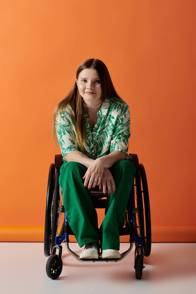 A young woman in a vibrant green outfit sits confidently in a wheelchair against a bright orange backdrop.